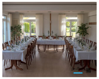 Festlich gedeckte Tafel in U-Form im charmanten P&uuml;tt&acute;s Gasthaus Langenberg mit wei&szlig;en Tischdecken, gef&auml;cherten Stoffservietten und Tischvasen mit Rosen, Lysianthus, Statice und Eukalyptus in Wei&szlig; und Violett