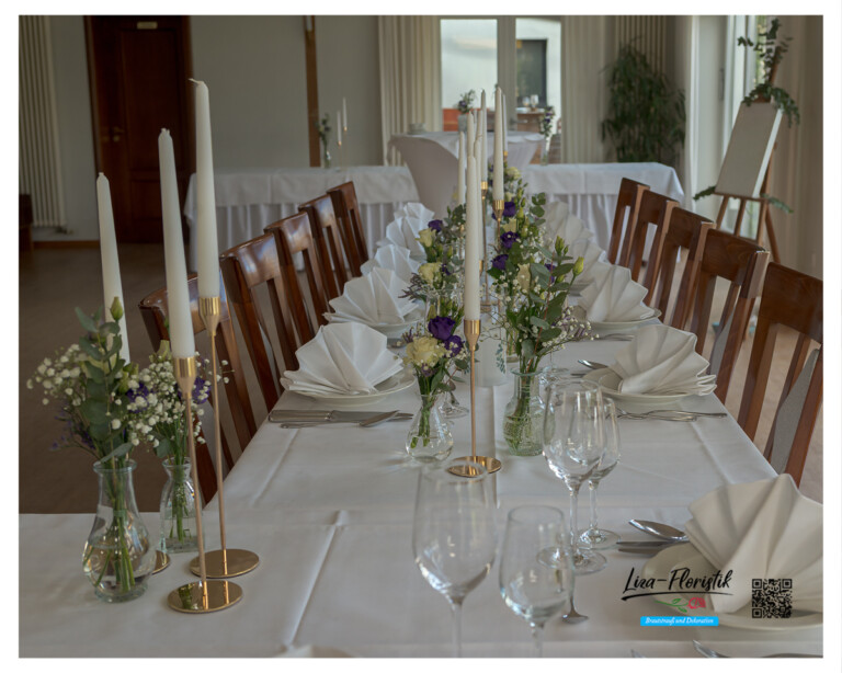 Romantisches Tischblumenarrangement mit goldenen Kerzenhaltern und einer Glasvase mit Rosen, Lysianthus, Statice und Eukalyptus in Weiß und Violett